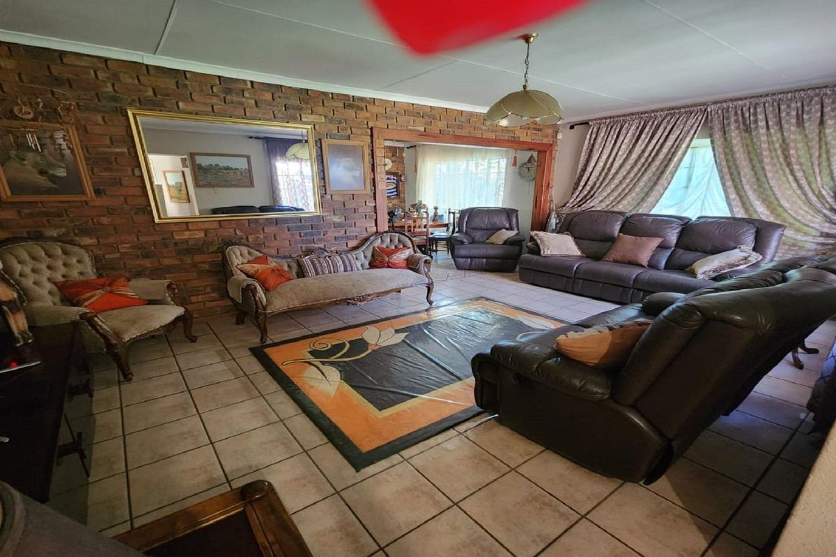 Spacious living room featuring a rustic exposed brick feature wall, tiled flooring, and large windows with curtains, offering a comfortable and traditional living space.
