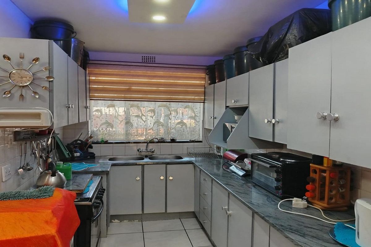 A functional kitchen featuring grey cabinetry, granite-style countertops, a double-basin sink, and integrated lighting, providing a practical workspace for daily meal preparation.