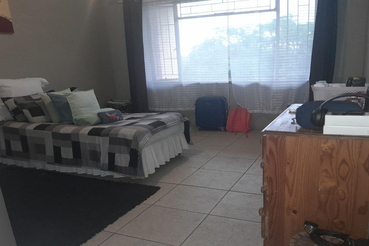 A bedroom featuring tiled flooring and a large window with security bars, providing natural light and a functional living space.