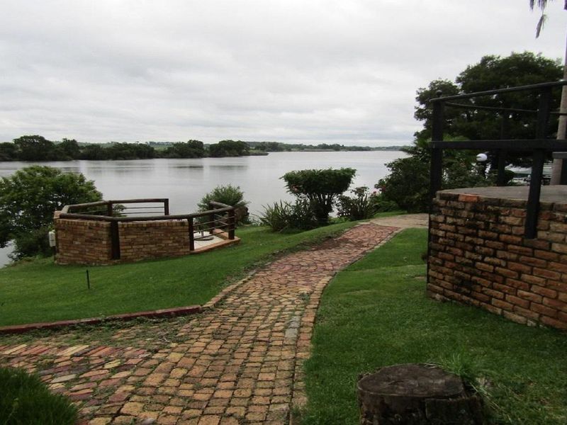 A scenic garden area featuring a brick-paved pathway leading towards a riverfront view with a built-in brick viewing deck.