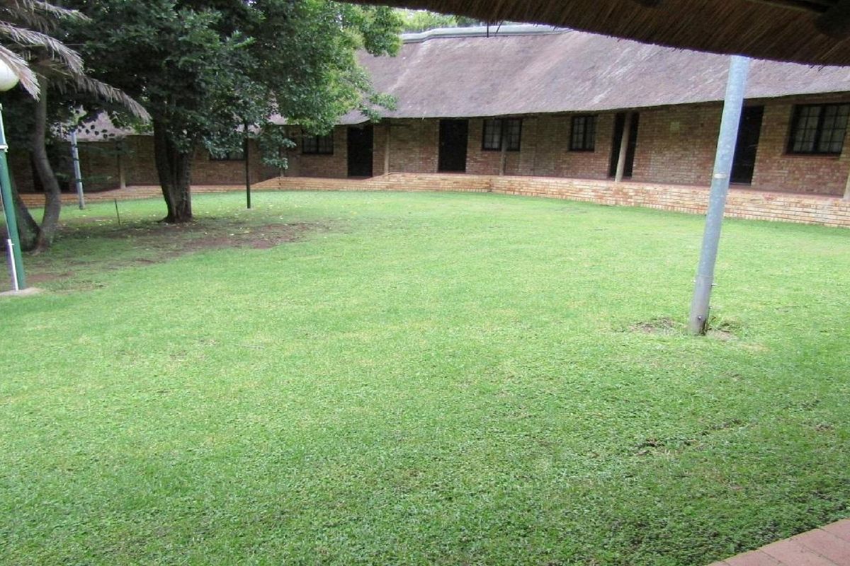 A view of a central lawn area surrounded by a brick-built residential building with a traditional thatched roof.