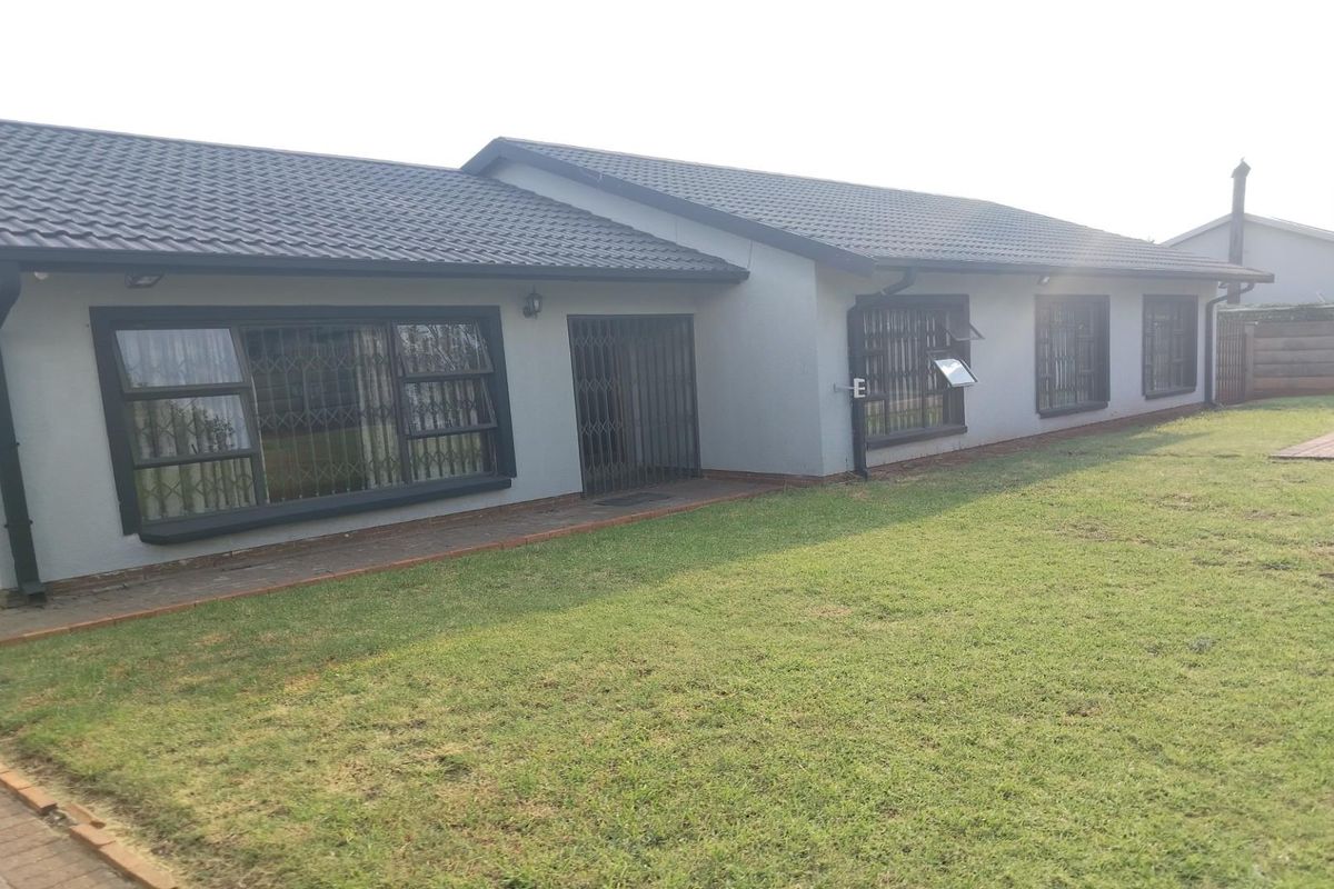 Rear view of the house featuring a tiled roof, grey exterior walls, security bars on windows, and a well-maintained lawn.