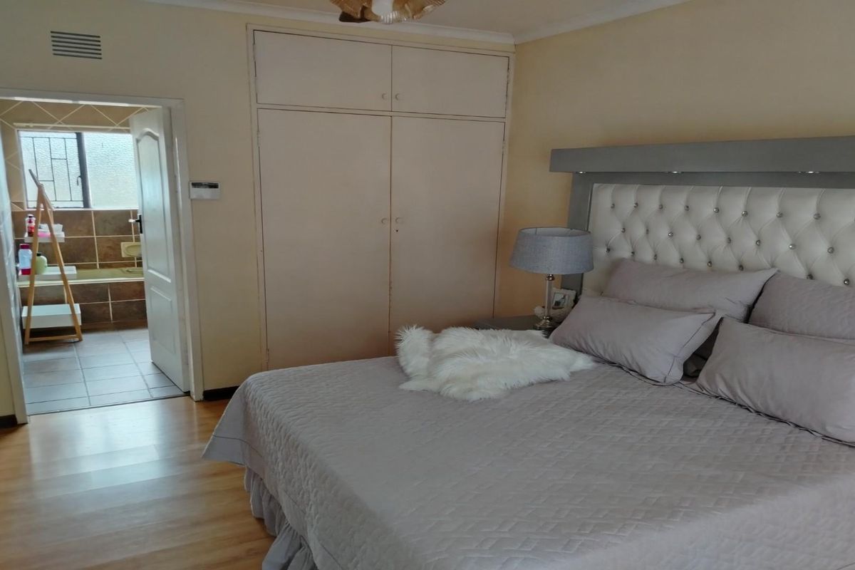 A bedroom featuring built-in cupboards and laminate flooring, with an adjoining bathroom visible through the doorway.