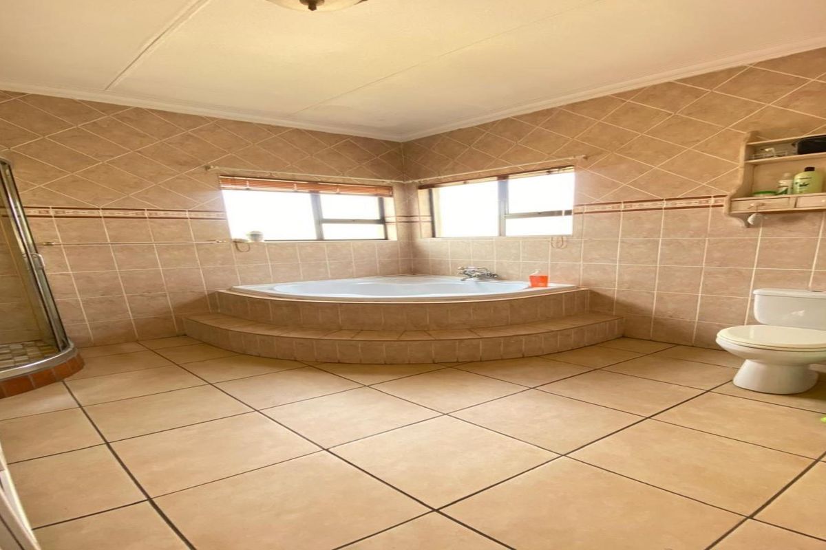 Spacious bathroom featuring a raised corner soaking tub, a separate glass-enclosed shower, and a standard toilet with neutral wall and floor tiling.