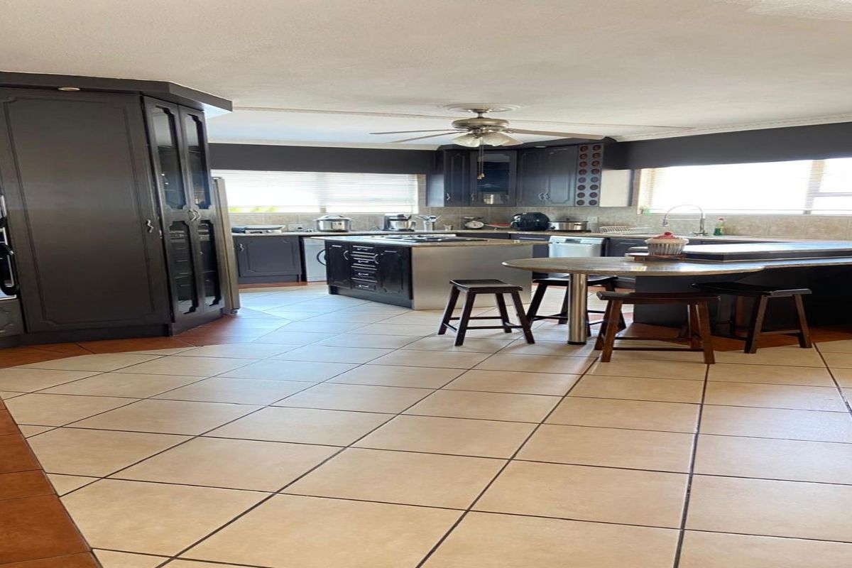 Spacious kitchen featuring dark cabinetry, a central island with integrated cooktop, tiled flooring, and a breakfast nook area.