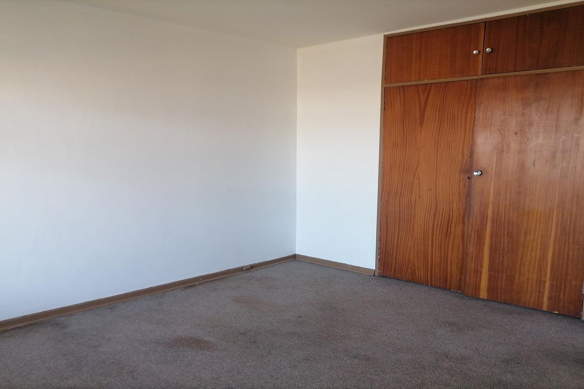A vacant bedroom featuring built-in wooden cupboards and carpeted flooring, offering a blank canvas for potential updates.