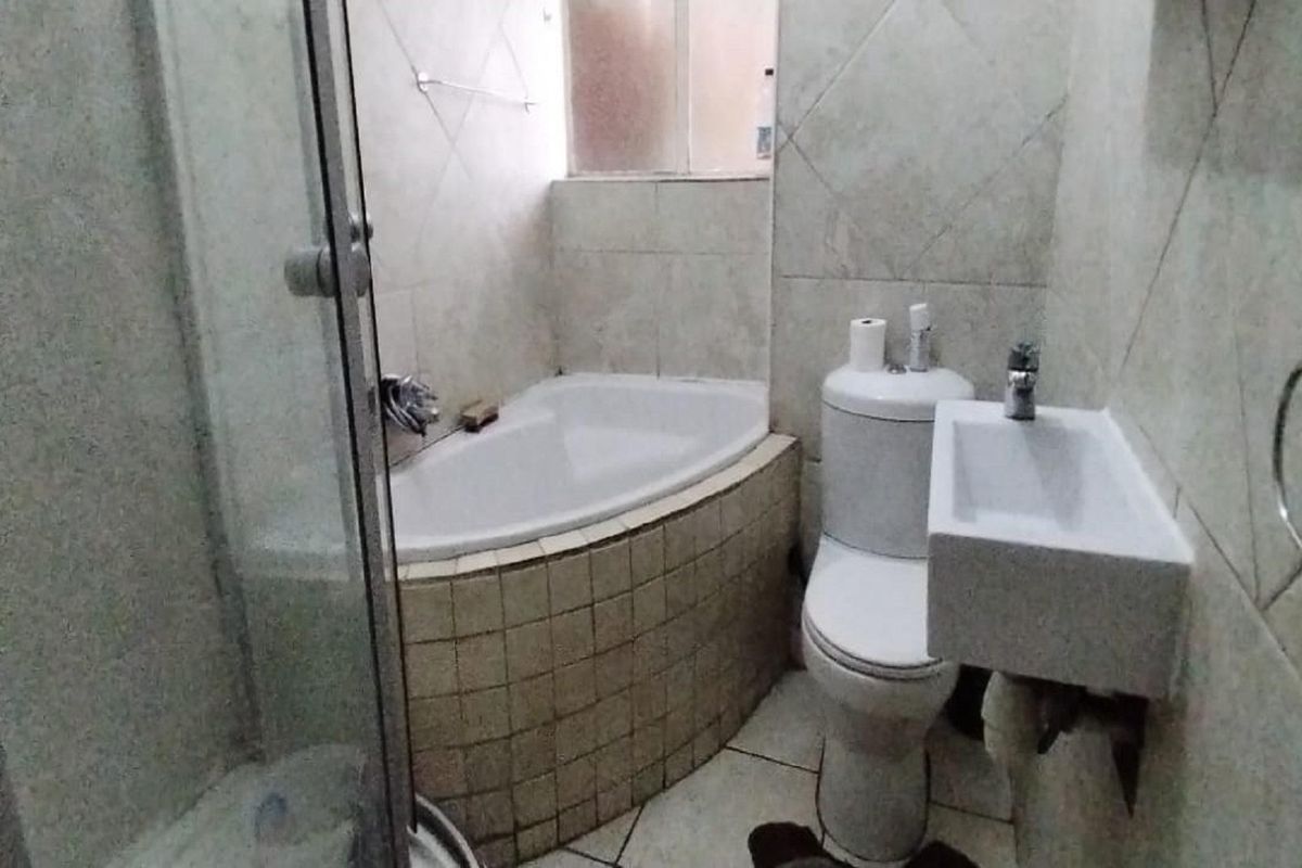 Compact bathroom featuring a corner bathtub, glass-enclosed shower, wall-mounted basin, and toilet with neutral wall and floor tiling.