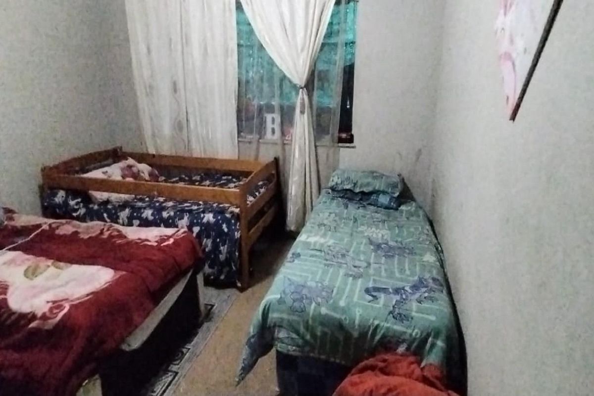 A functional bedroom space featuring a window with curtains and standard flooring, suitable for multiple beds.