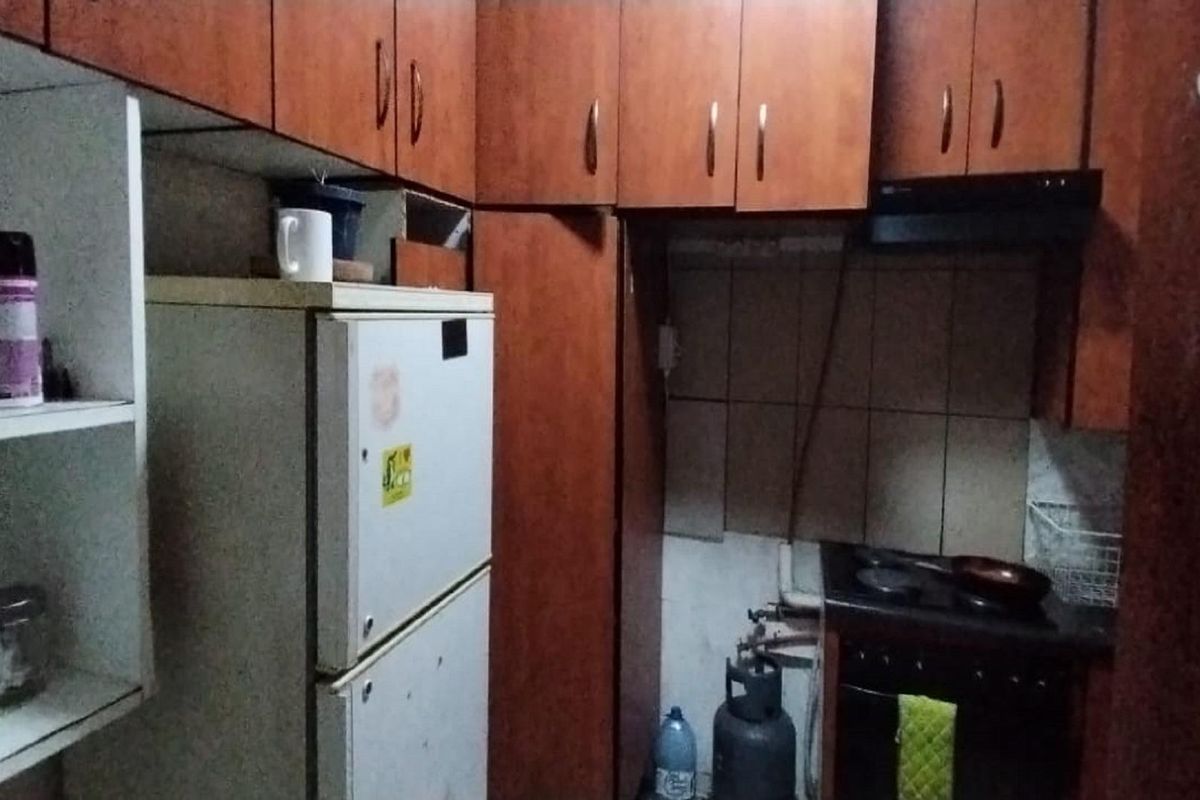 A compact kitchen featuring wooden cabinetry, a built-in stove with extractor fan, and tiled splashbacks in a dated, functional layout.
