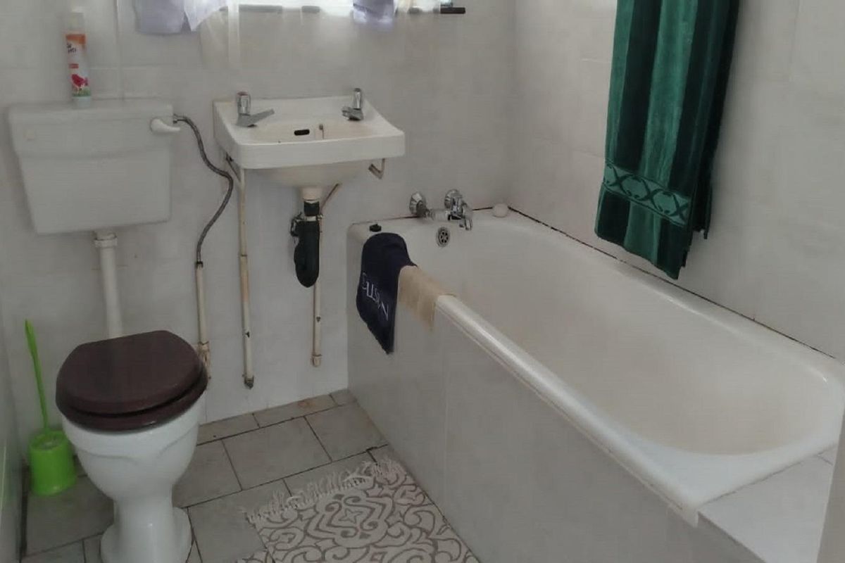 A compact bathroom featuring a standard bathtub, wall-mounted basin, and toilet with white wall tiling throughout.