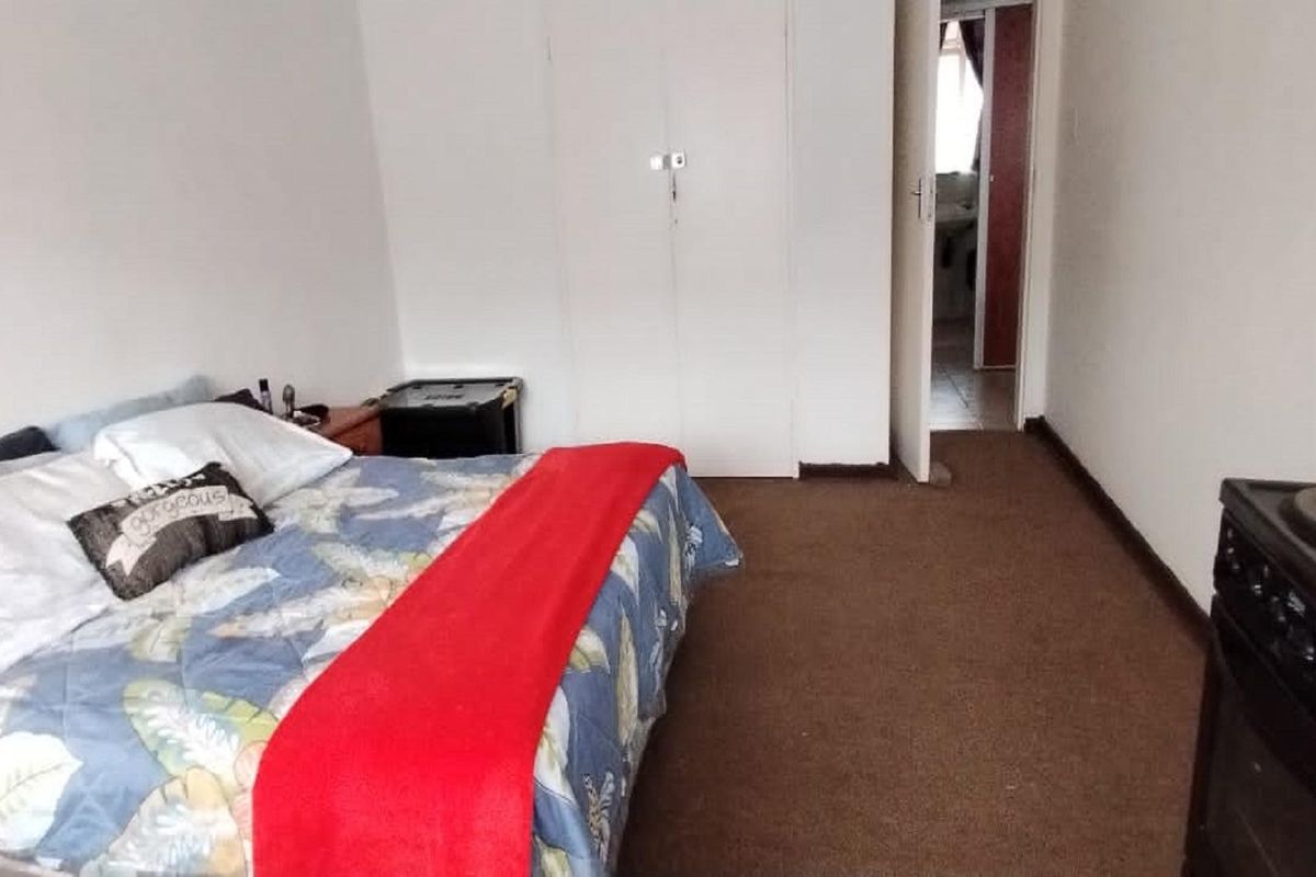 A bedroom featuring built-in cupboards and carpeted flooring, with an adjacent doorway leading to a bathroom area.