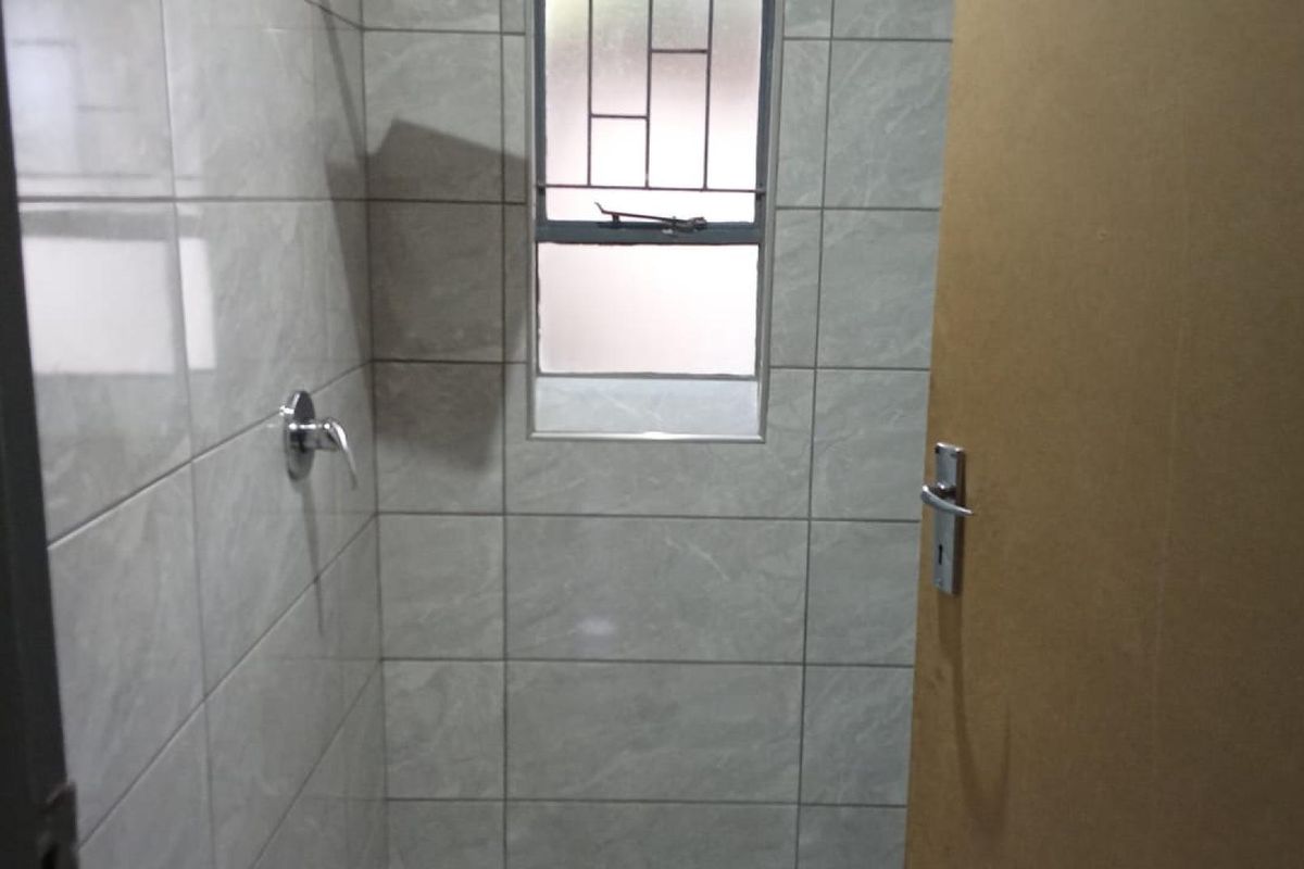 A tiled bathroom shower area featuring a window with security bars and a standard interior door.
