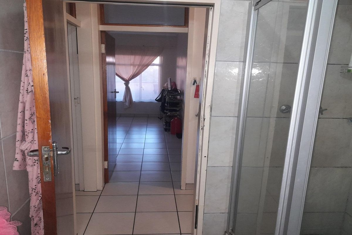 A view from a tiled bathroom looking through a doorway into an adjacent room with tiled flooring and natural light.