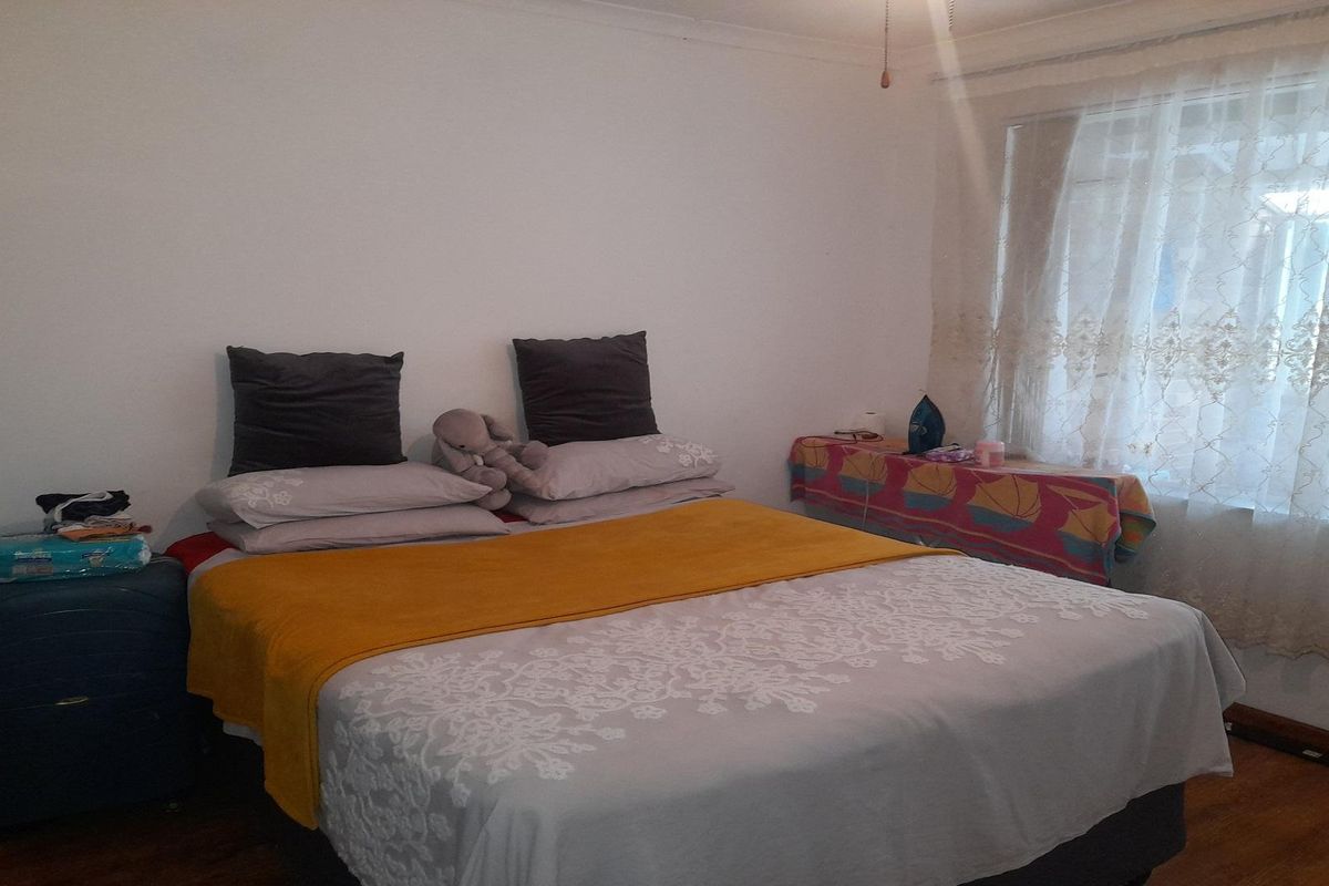 A bedroom featuring laminate flooring and a window with sheer curtains.