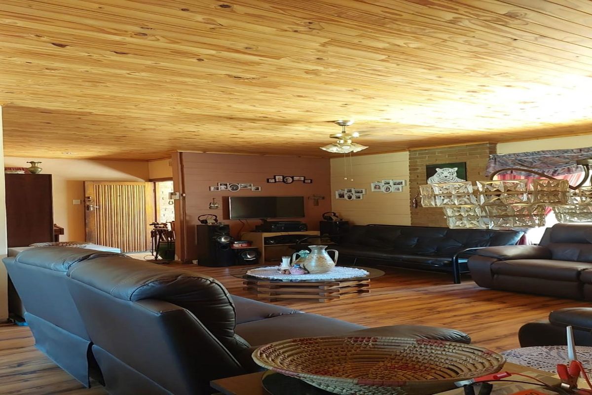 Spacious living area featuring natural timber ceiling paneling, exposed brick accent wall, and timber flooring, creating a warm and rustic atmosphere.