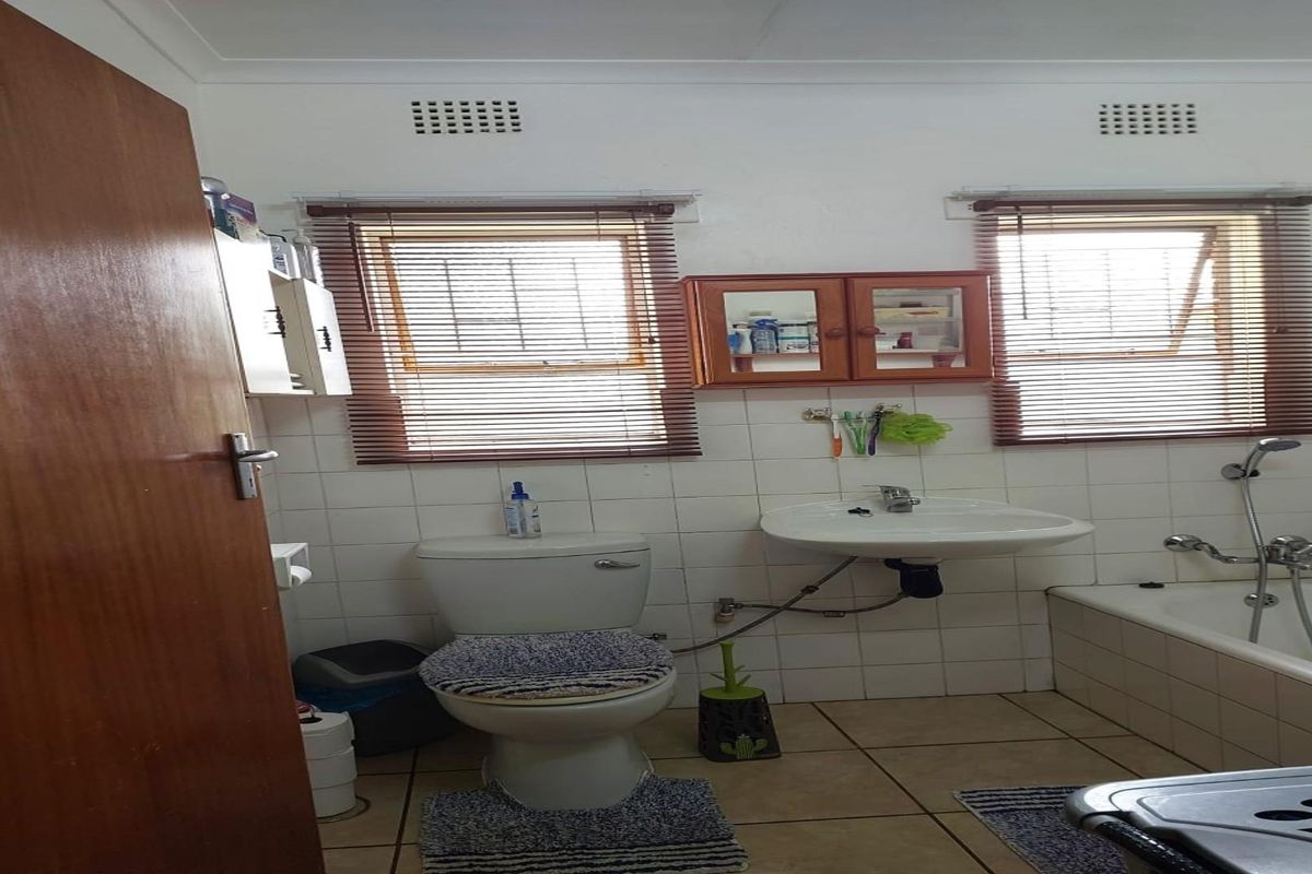 A functional bathroom featuring a standard toilet, wall-mounted basin, and a bathtub with a shower mixer, finished with tiled flooring and walls.