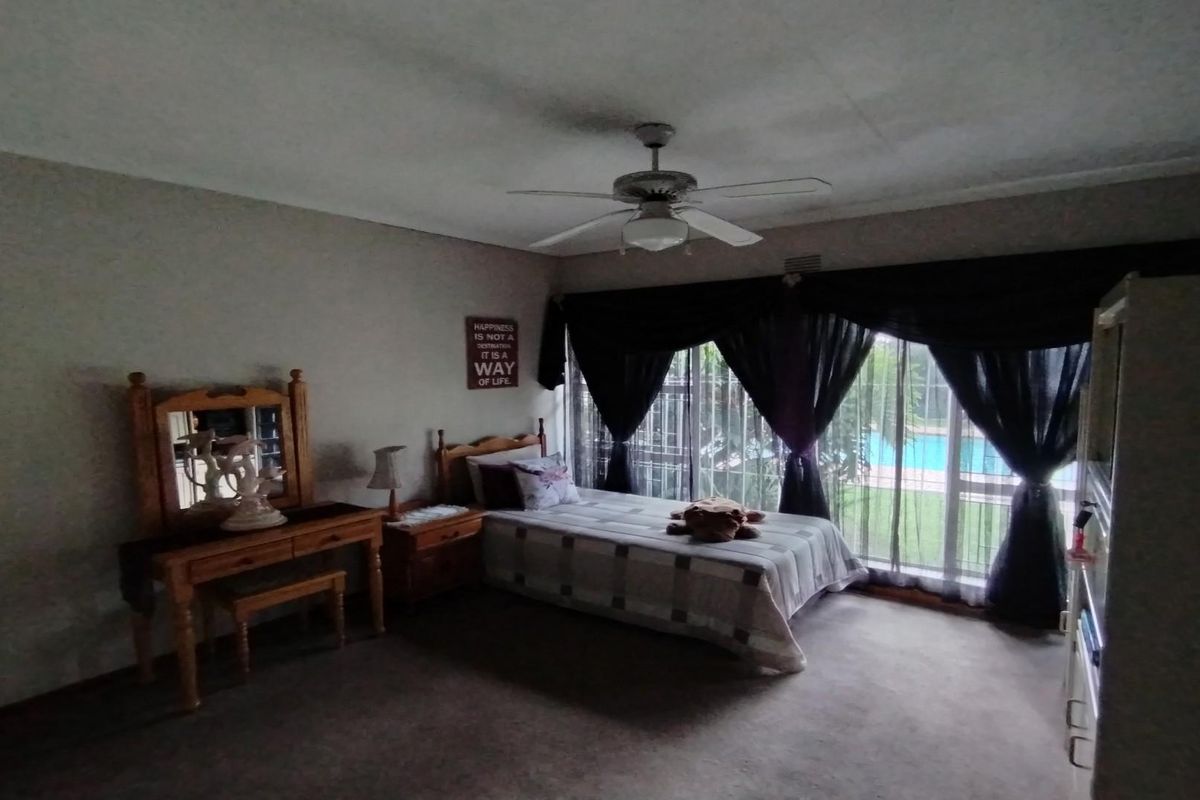 A spacious bedroom featuring carpeted flooring, a ceiling fan, and large sliding glass doors that provide natural light and views of the pool area.