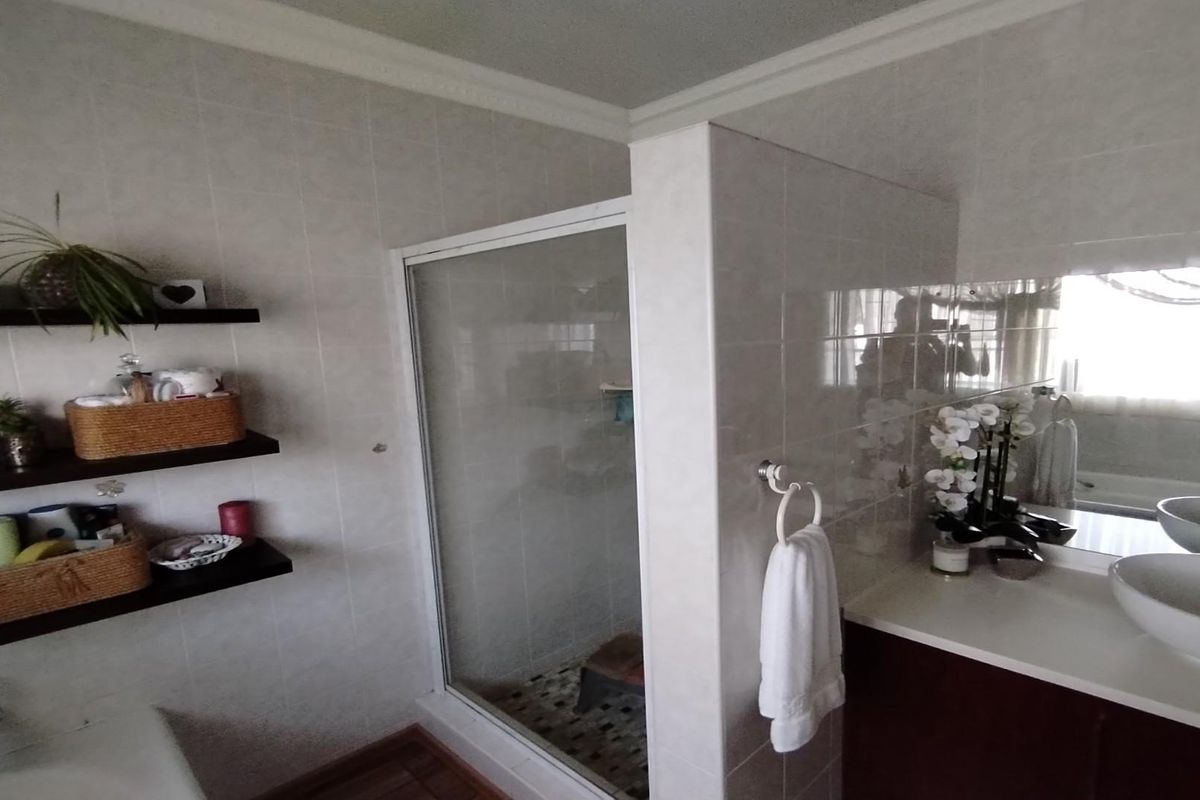 A functional bathroom featuring a glass-enclosed shower, a vanity with a vessel sink, and wall-mounted shelving for storage.