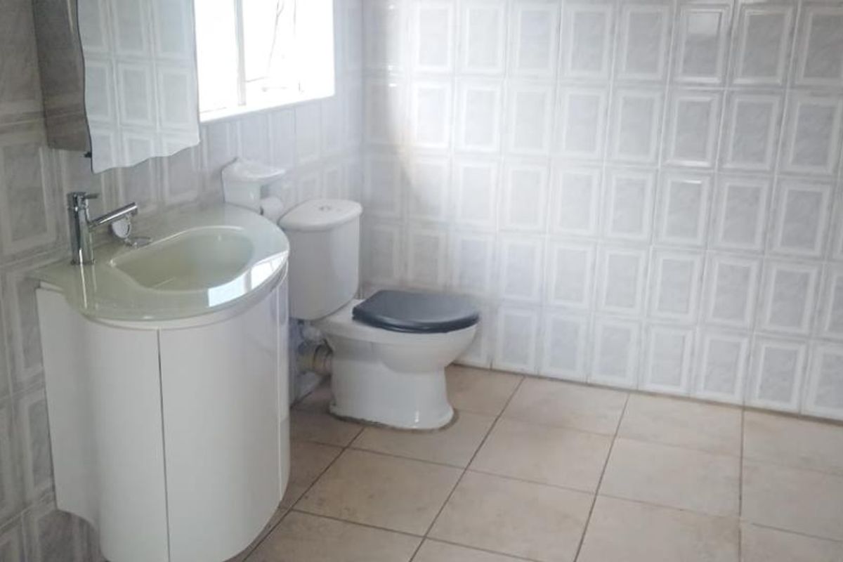 A functional bathroom featuring a vanity basin, toilet, and fully tiled walls and floors.