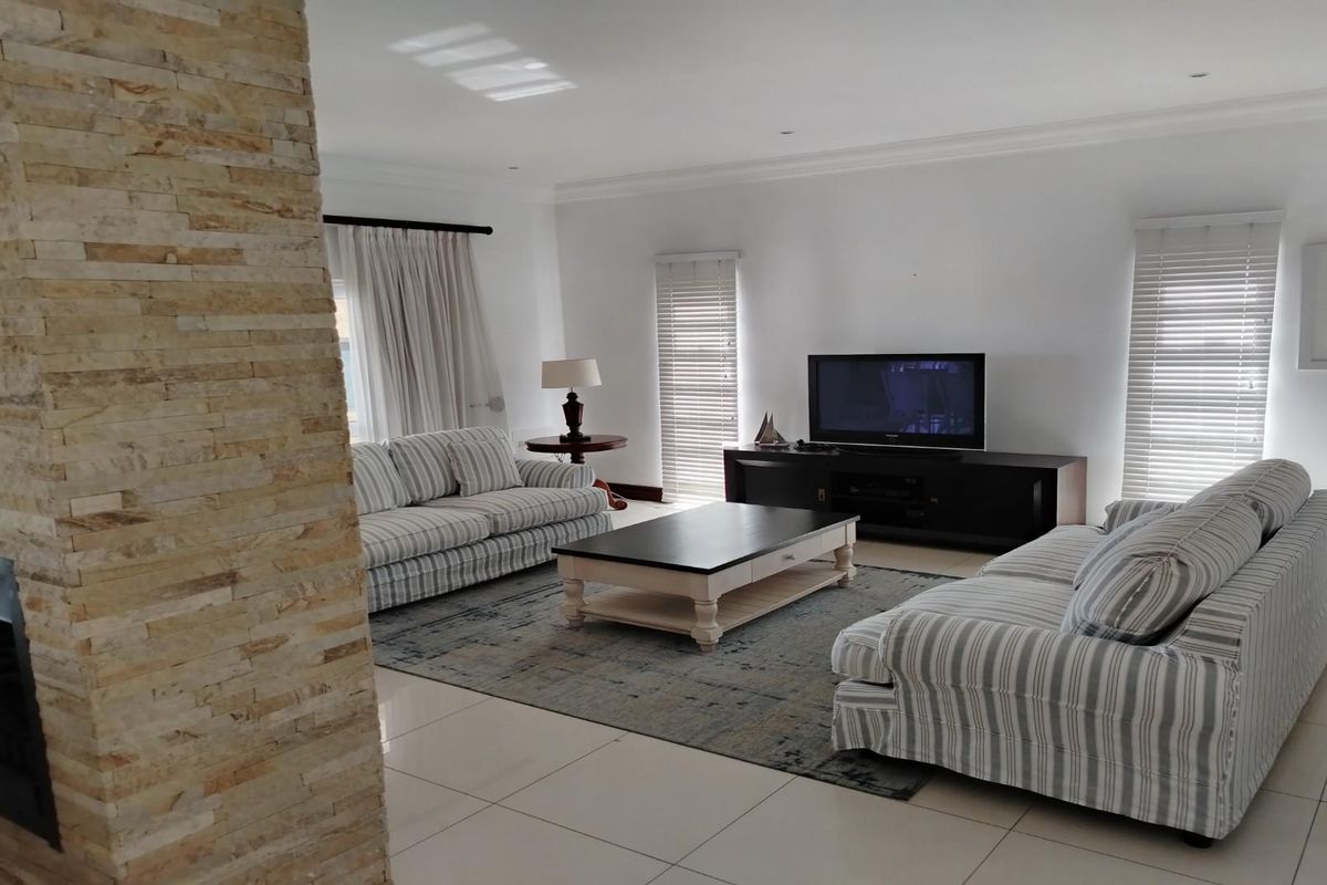 Spacious living room featuring a prominent stone-clad fireplace feature wall, tiled flooring, and large windows with fitted blinds.