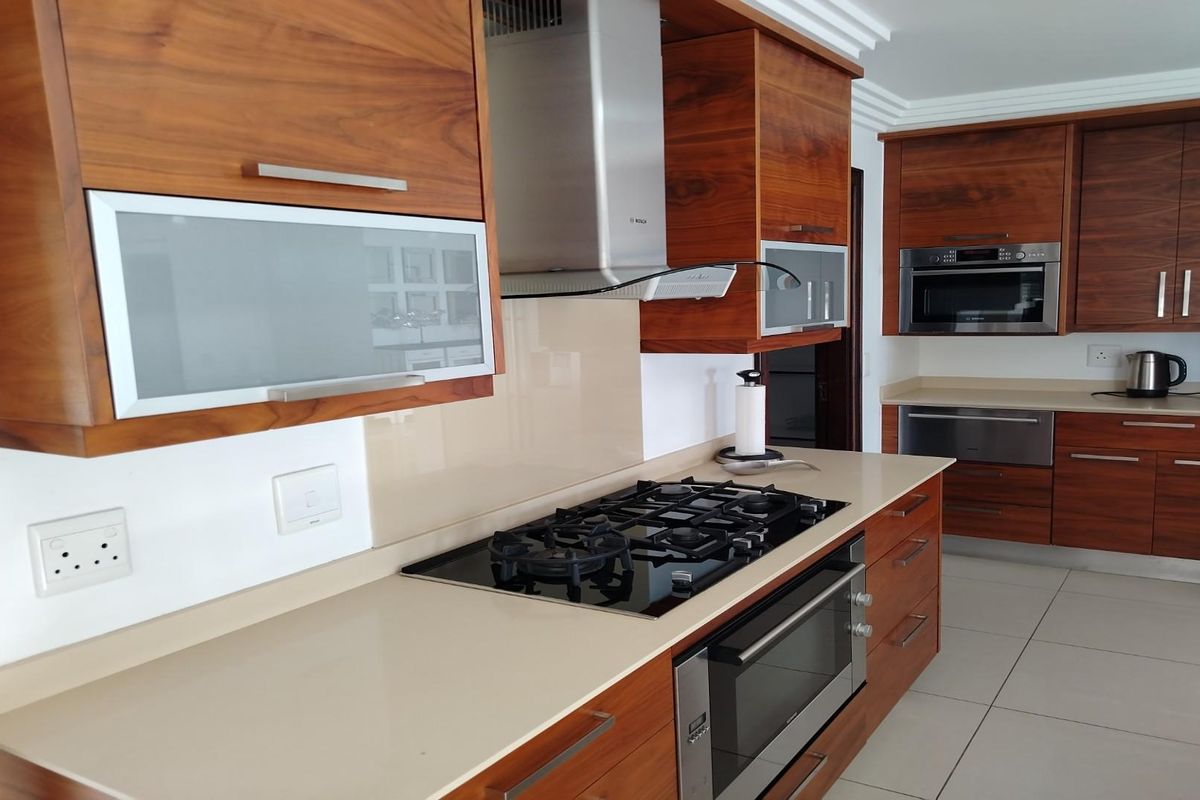 Modern kitchen featuring rich wood cabinetry, stone countertops, a built-in gas hob, stainless steel extractor fan, and integrated oven and microwave.
