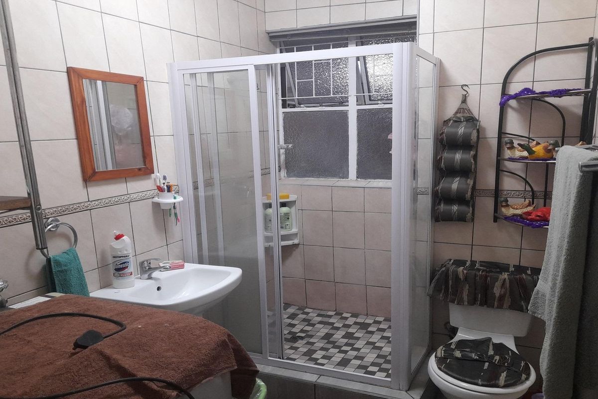 A functional bathroom featuring a corner shower enclosure, pedestal basin, and toilet, finished with neutral wall tiles and a classic layout.