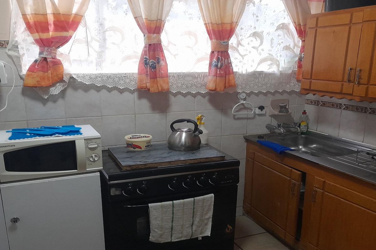 A compact kitchen featuring wooden cabinetry, a tiled backsplash, a stainless steel sink, and a freestanding stove.