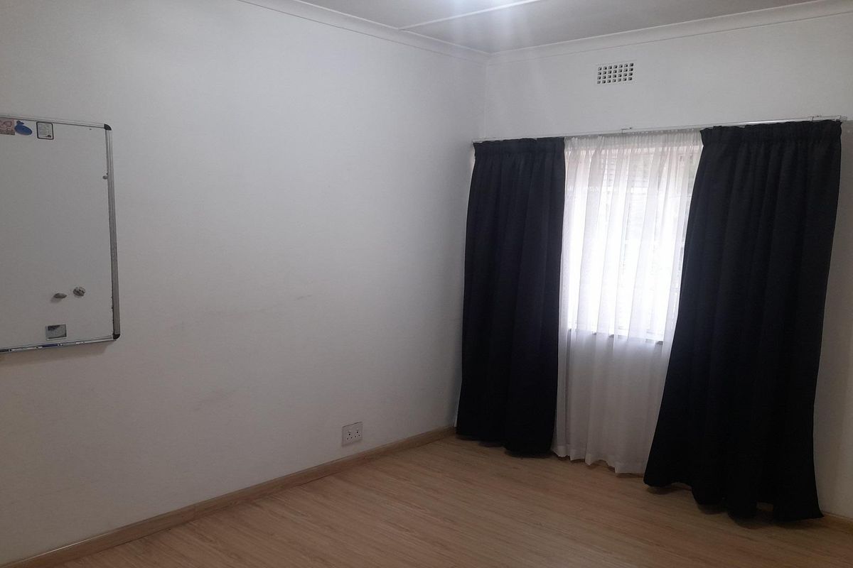 A simple bedroom featuring light wood-look flooring, white walls, and a window with curtain tracks.