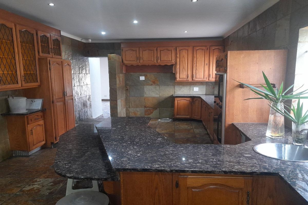 Spacious kitchen featuring dark granite countertops, extensive wooden cabinetry, and natural stone wall finishes with integrated oven and sink.