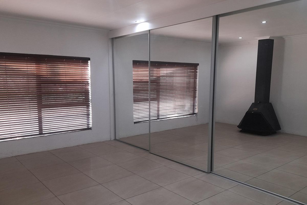 Spacious living area featuring large mirrored sliding wardrobe doors, tiled flooring, and a built-in black metal fireplace.