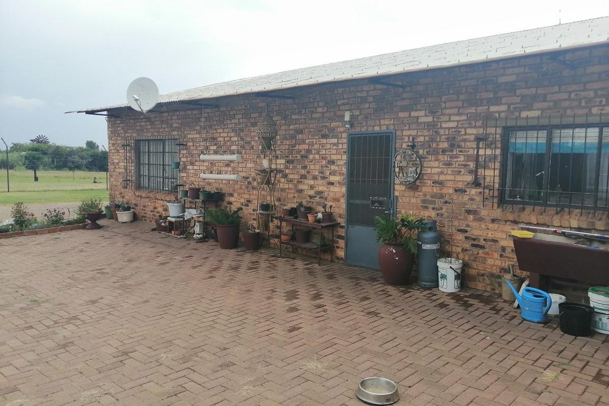 Rear exterior view of a brick-built small holding dwelling featuring a paved patio area, security bars on windows, and a metal security door.