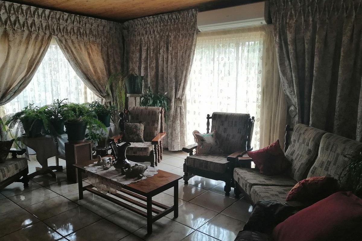 A living room featuring tiled flooring, a wooden ceiling, and a wall-mounted air conditioning unit, with large windows providing natural light.
