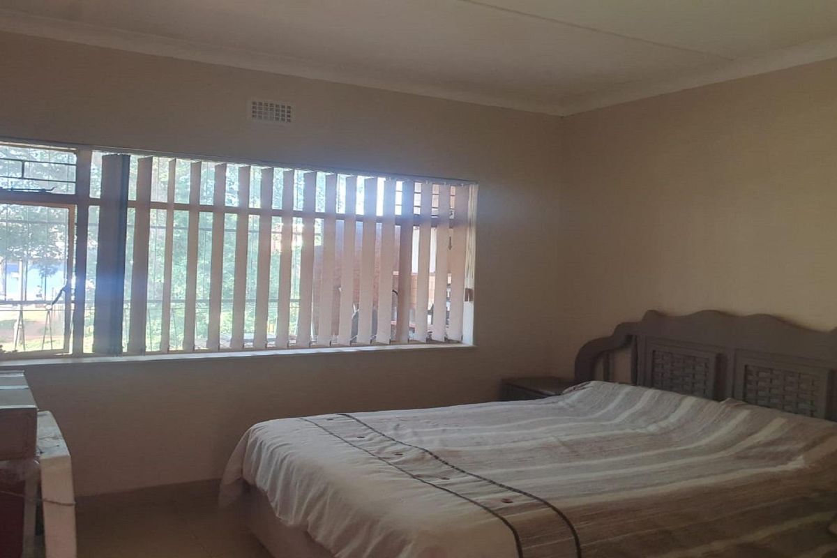 A spacious bedroom featuring a large window with vertical blinds, providing natural light and a view of the exterior surroundings.