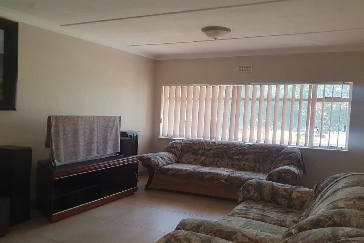 A spacious living room featuring tiled flooring, large windows with vertical blinds, and a ceiling-mounted light fixture.