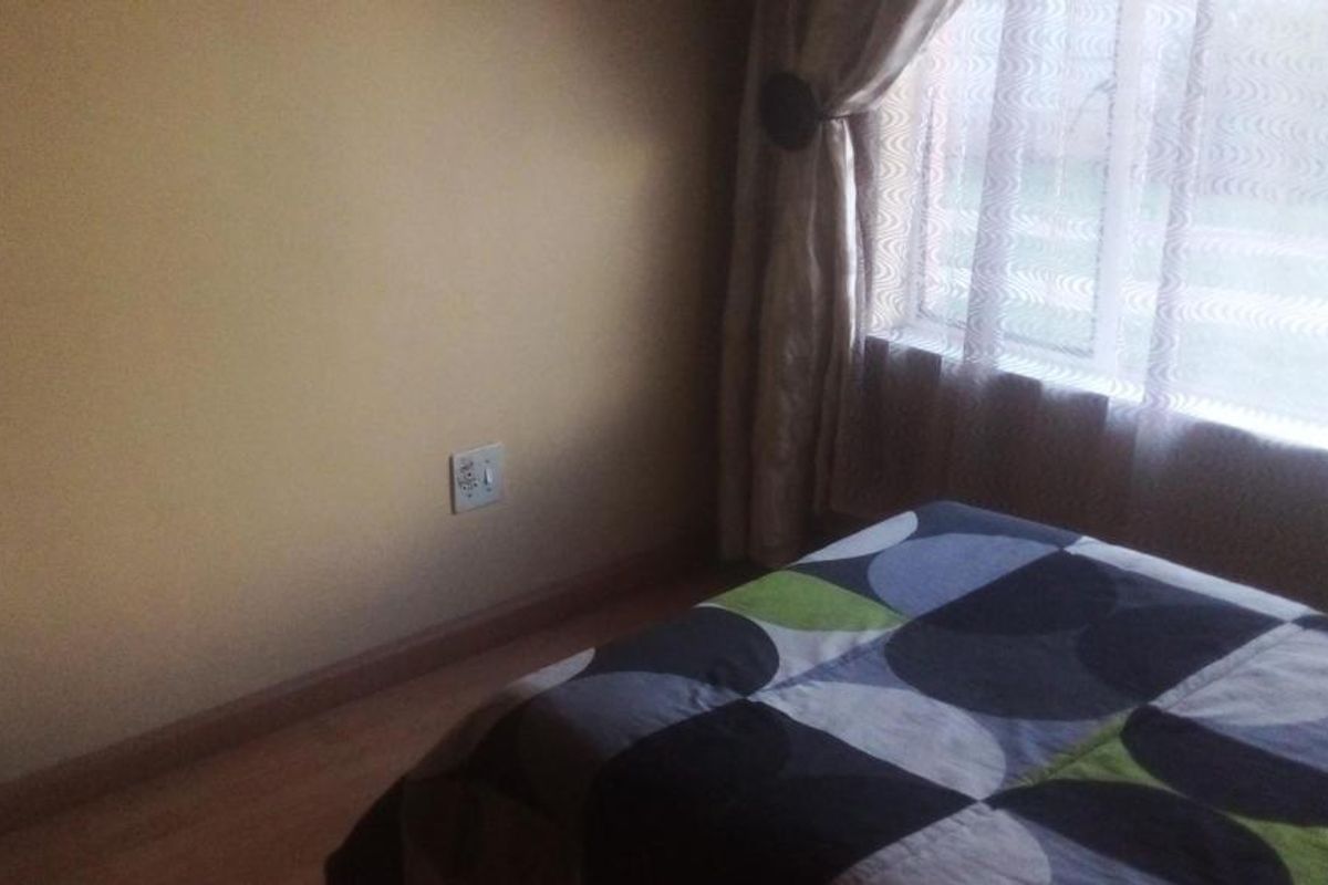 A bedroom featuring laminate flooring and a window with curtains, providing a simple and functional living space.