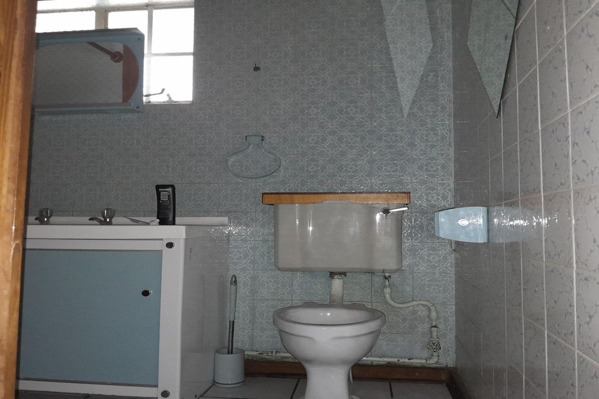 A dated bathroom featuring a standard toilet, vanity basin, and tiled walls, requiring modernization and cosmetic updates.