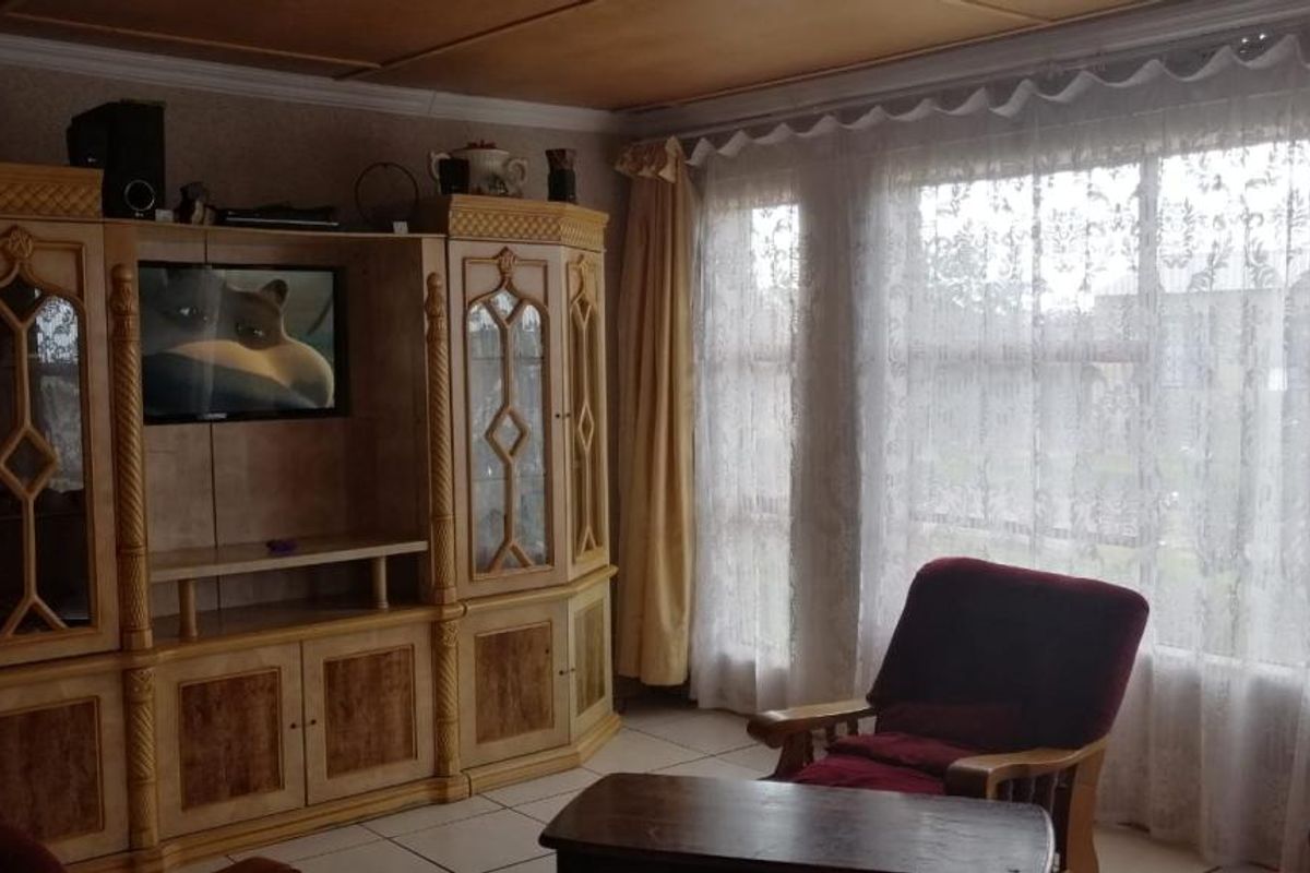 A living room featuring large windows with natural light, tiled flooring, and a built-in wooden wall unit.