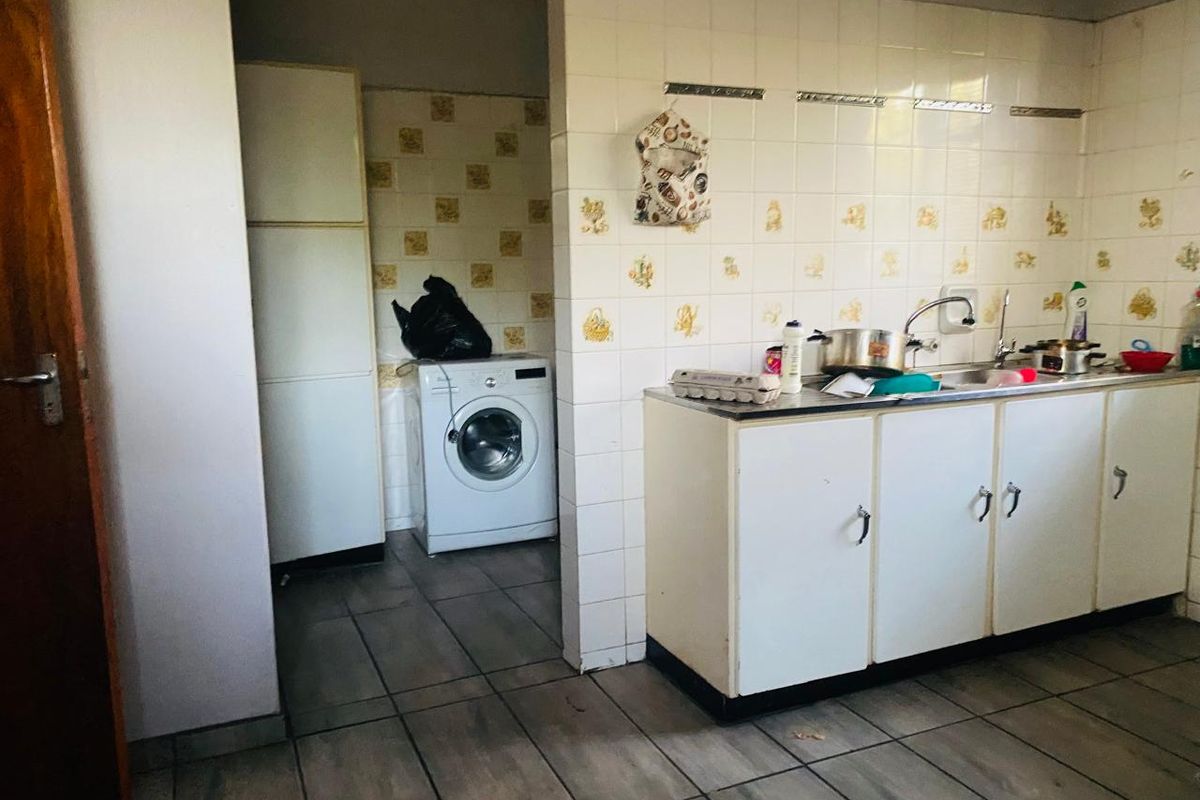 A functional kitchen area featuring tiled splashbacks, built-in cabinetry, and a stainless steel sink, with an adjacent laundry space.