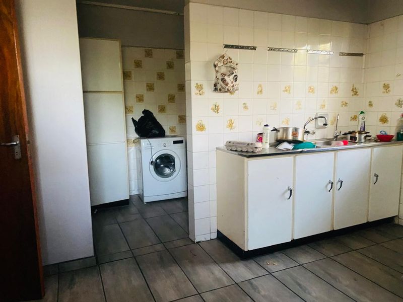 A functional kitchen area featuring tiled splashbacks, built-in cabinetry, and a stainless steel sink, with an adjacent laundry space.