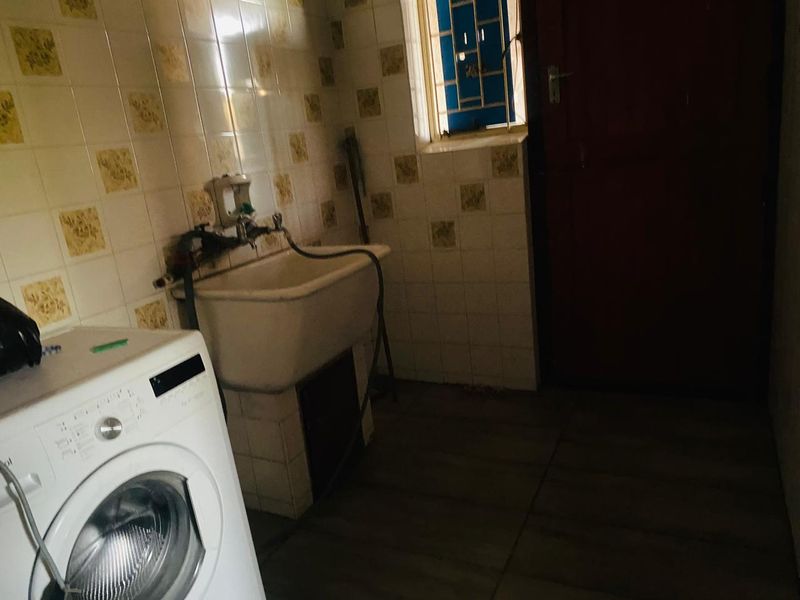 A functional laundry area featuring a utility sink, tiled walls, and tiled flooring, providing a practical space for household chores.