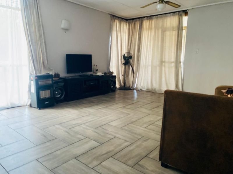 Spacious living room featuring modern herringbone tile flooring, a ceiling fan, and large windows with curtains allowing for natural light.