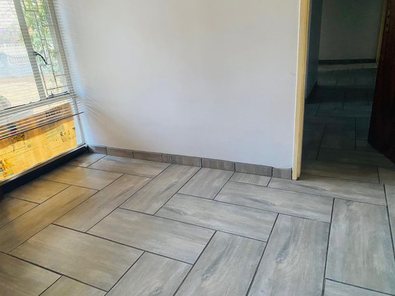 An empty living area featuring modern grey wood-look floor tiles laid in a herringbone pattern and fitted venetian blinds.