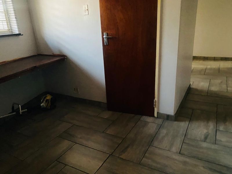 A functional hallway or utility space featuring tiled flooring, a built-in desk area, and a wooden door leading to an adjacent room.