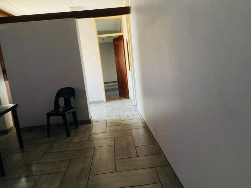 A simple hallway featuring tiled flooring and a wooden door leading to an adjacent room.