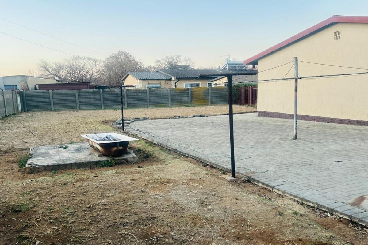 A spacious rear garden featuring a paved patio area, perimeter boundary wall, and a large open lawn space.