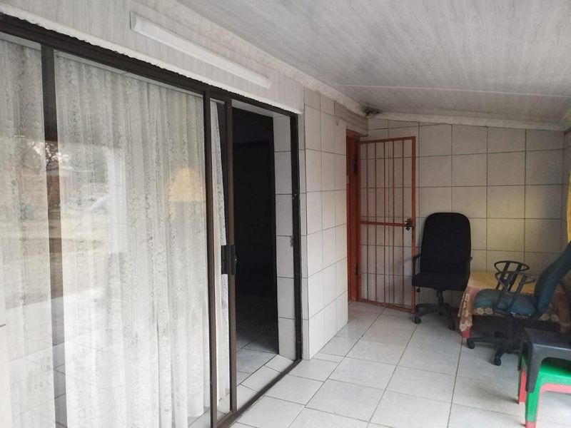 A covered patio area featuring tiled flooring, tiled walls, and a sliding glass door entrance, providing a functional outdoor transition space.