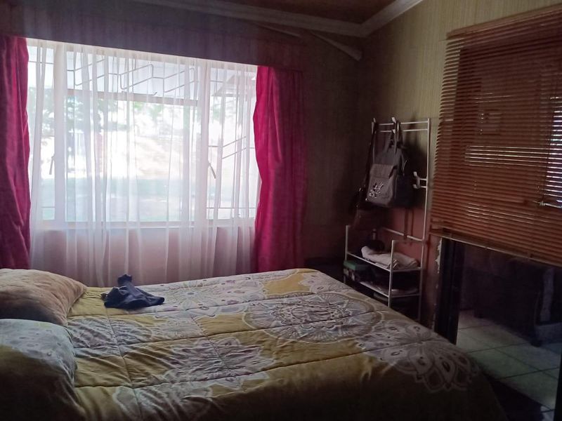 A bedroom featuring tiled flooring, a large window with security bars, and wooden blinds, offering a functional space with natural light.