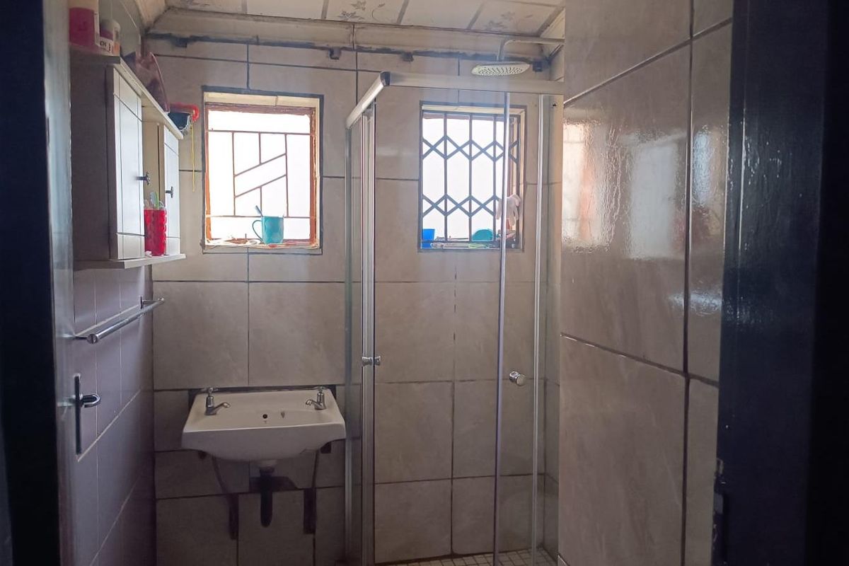 A compact bathroom featuring a wall-mounted basin, a glass-enclosed shower, and tiled walls with security bars on the windows.