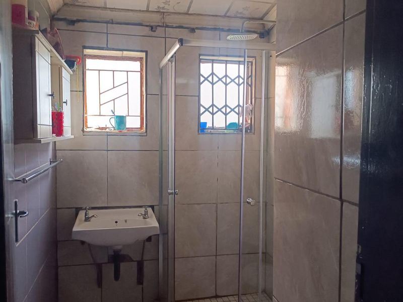 A compact bathroom featuring a wall-mounted basin, a glass-enclosed shower, and tiled walls with security bars on the windows.