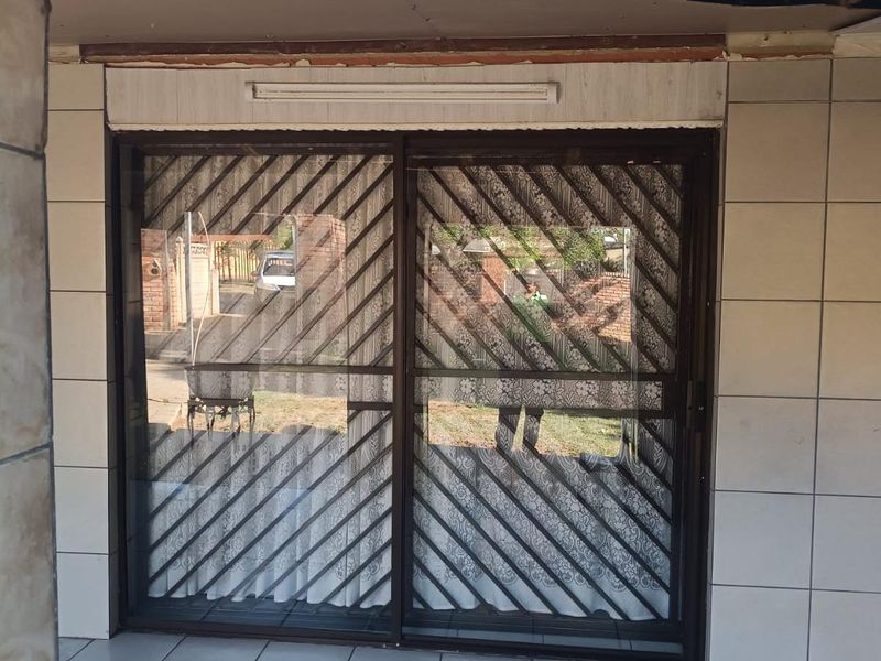 A covered patio area featuring tiled walls and flooring with a sliding glass door and integrated security gate.